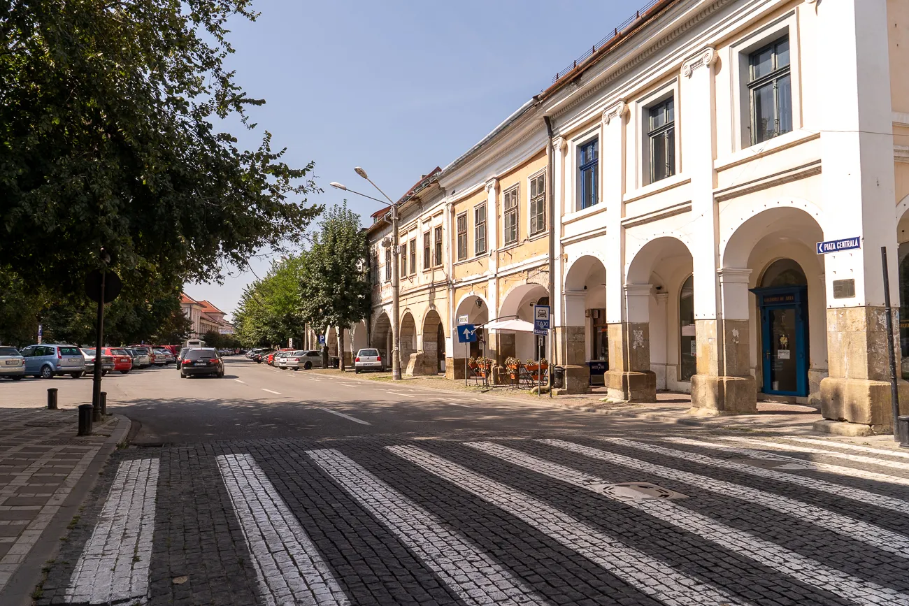 Straße mit Arkadenhaus und Fußgängerüberweg unter Bäumen