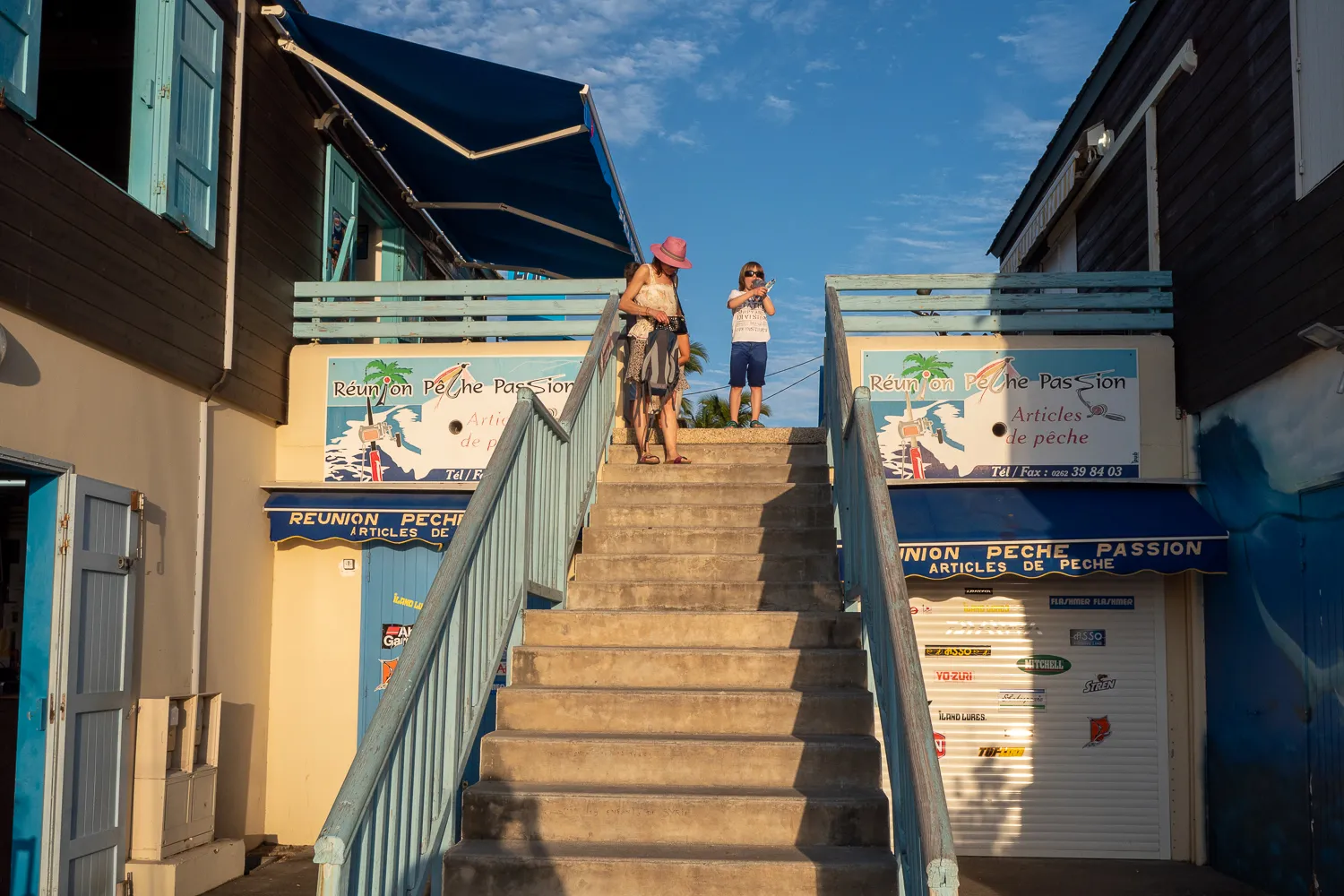 Zwei Personen steigen eine Außentreppe zwischen Fischgeschäften an einem Strandort hinauf.