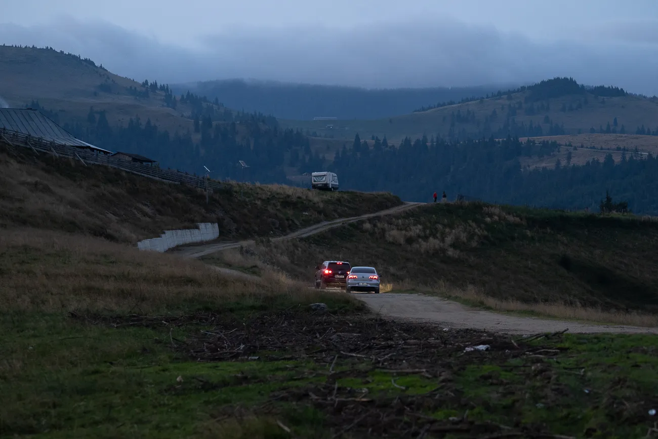 Zwei Autos fahren auf einer unbefestigten Straße durch eine bergige Landschaft.