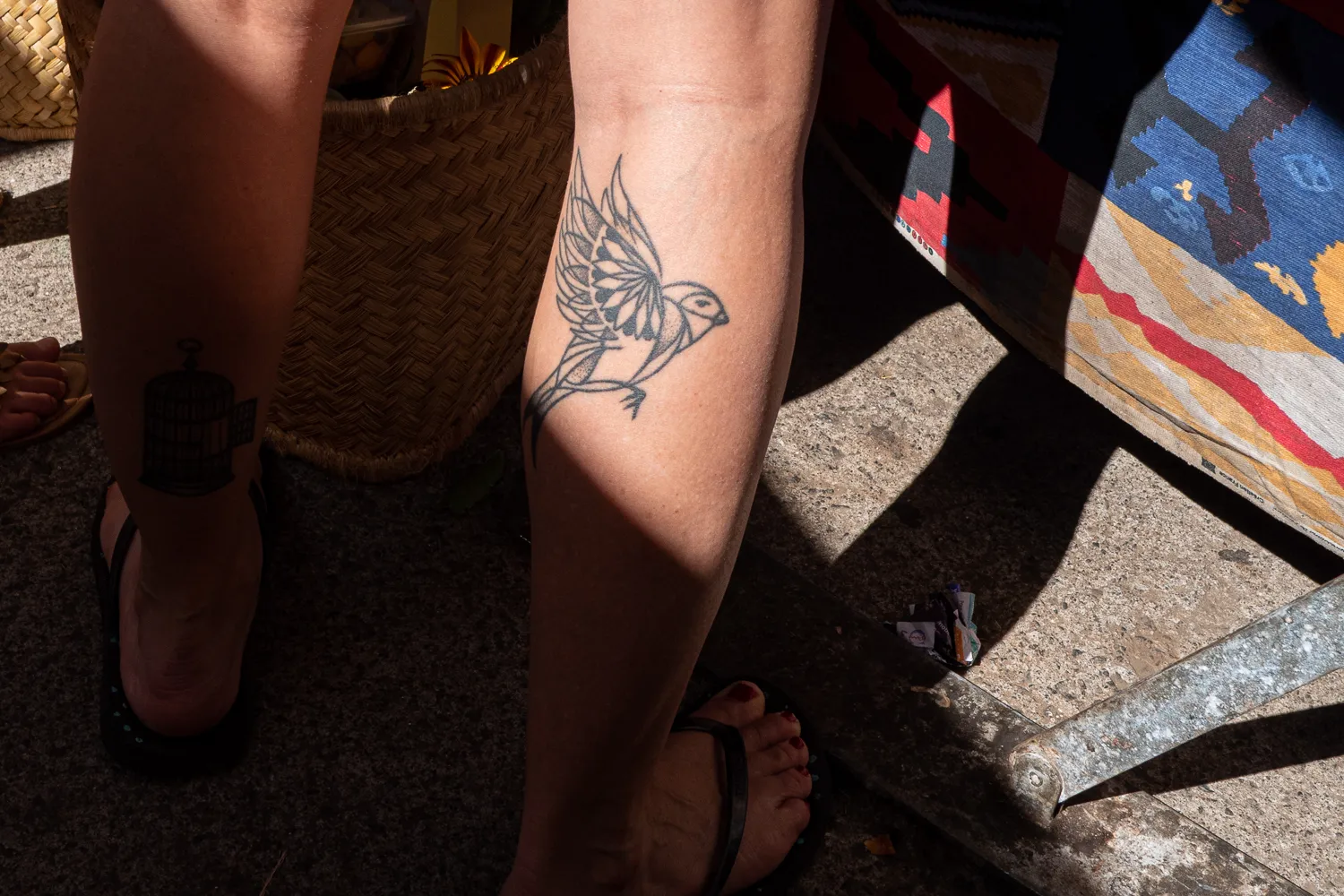 Bein mit Vogel- und Käfigtattoo im Sonnenlicht