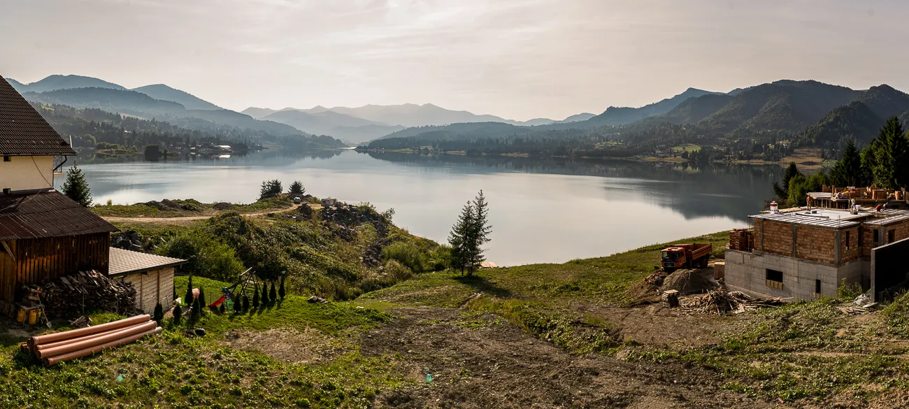Blick auf einen See mit Bergen im Hintergrund und Bauernhof im Vordergrund