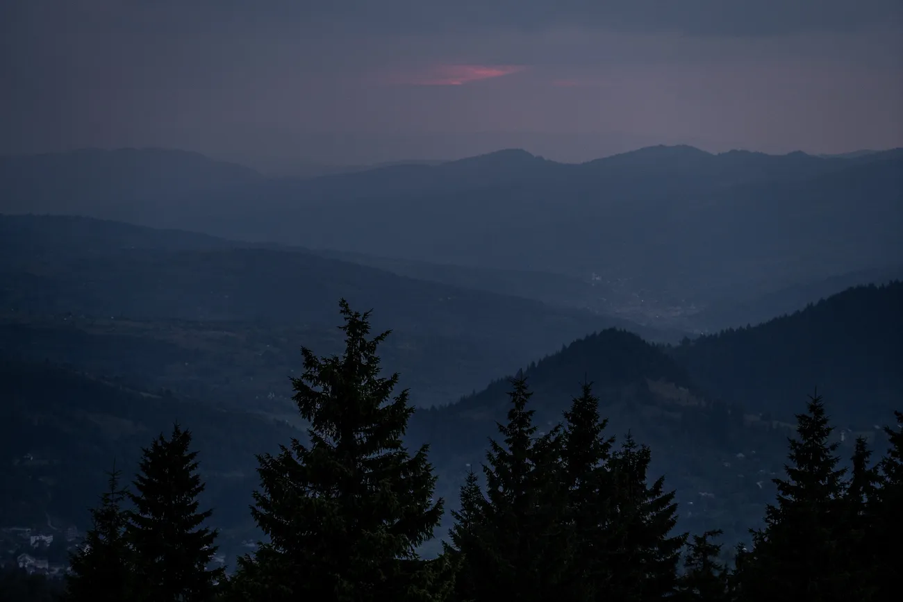 Dämmerung über bewaldeten Bergen mit rosa Wolken am Horizont