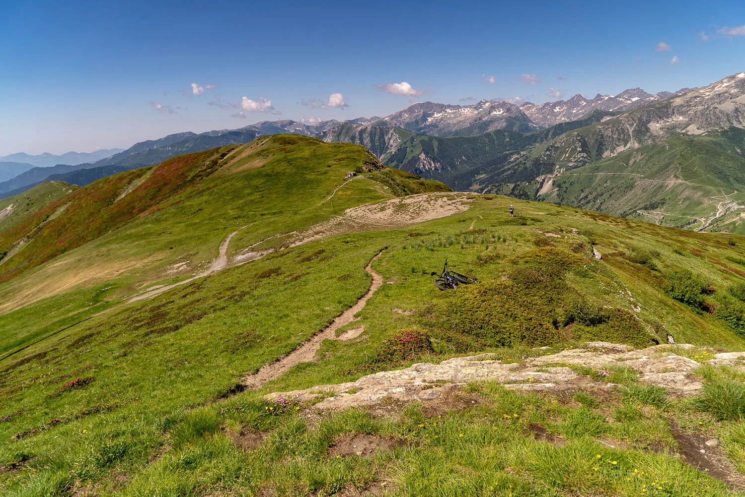 grüne bergwiese mit wanderrouten und fernen gipfeln unter blauem himmel