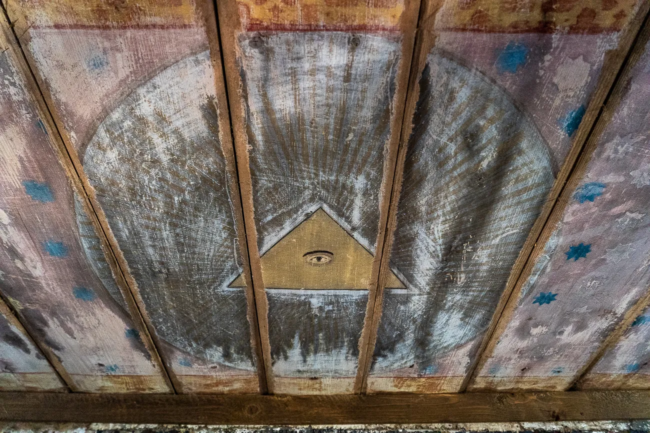 Alter Deckenbalken mit abblätternder Farbe und einem Auge in Dreieck.