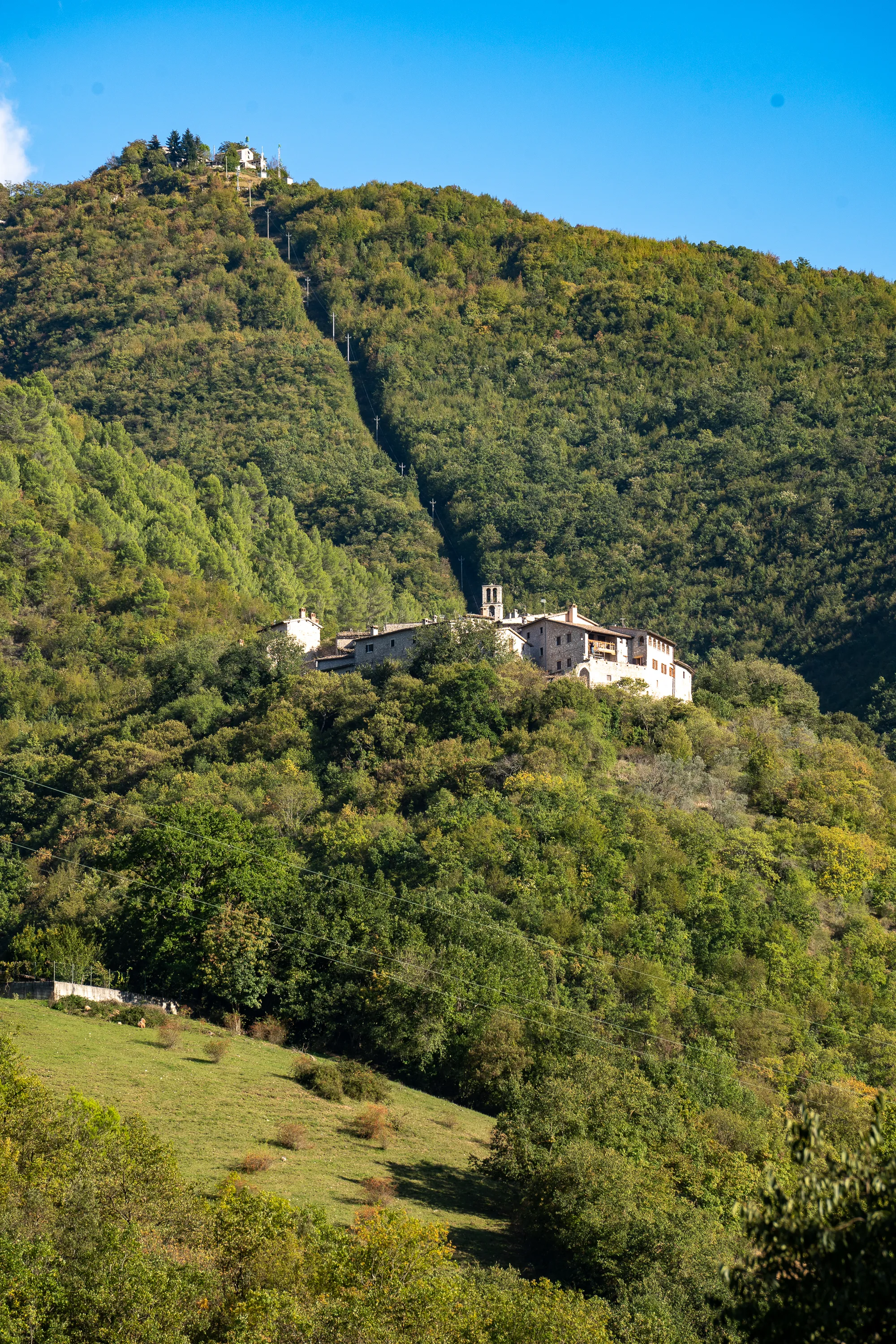Dorf auf grüner Hügellandschaft mit Steinhaus und Kirche unter blauem Himmel