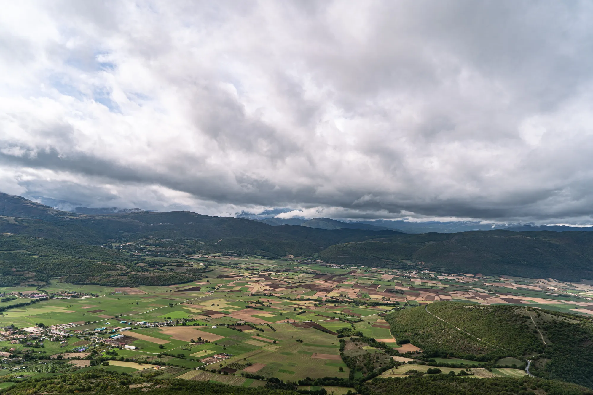 Weite Landschaft mit Feldern, Bergen und bewölktem Himmel
