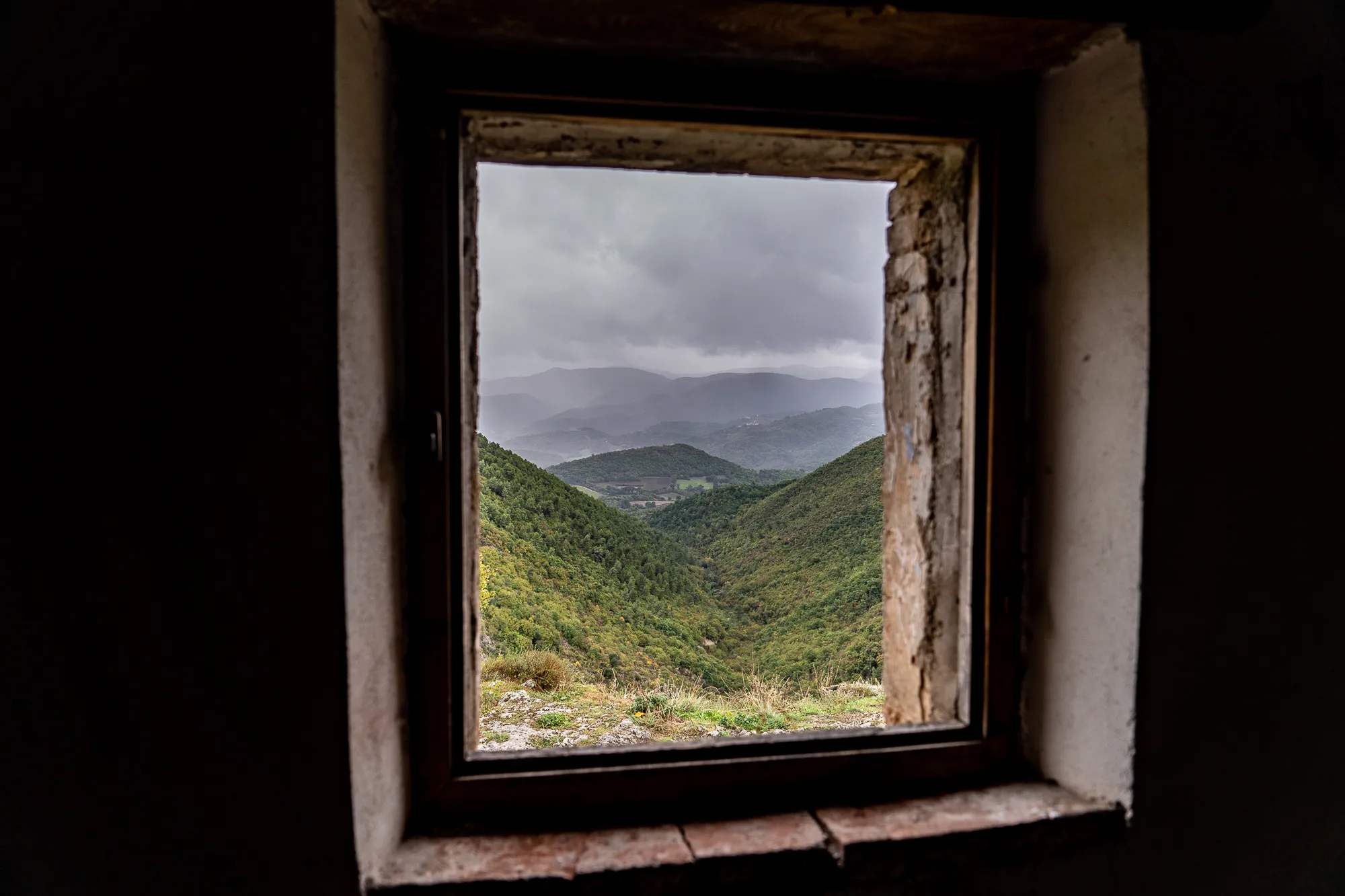 Blick durch altes Fenster auf grüne Berge und bewölkten Himmel