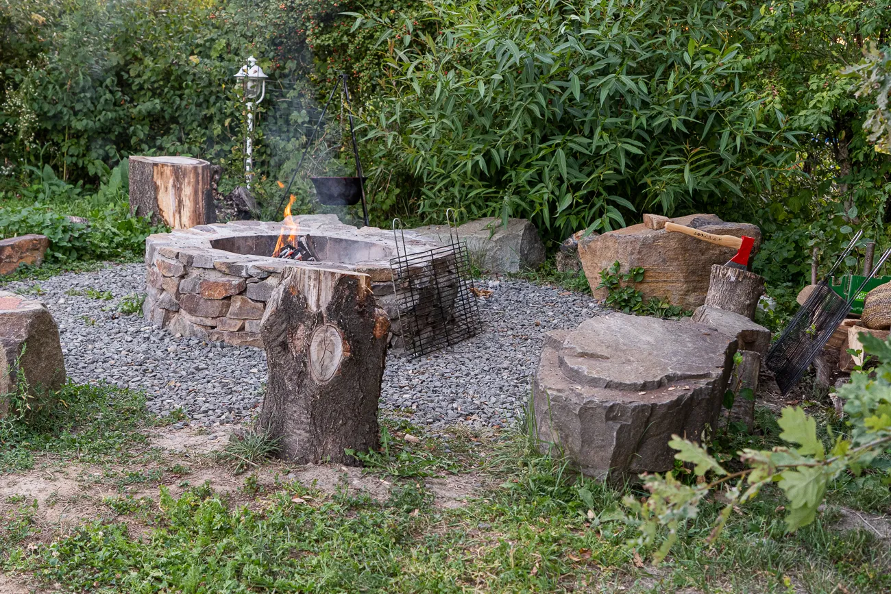 Feuerstelle mit Steinring und Baumstümpfen im Gras und Kies