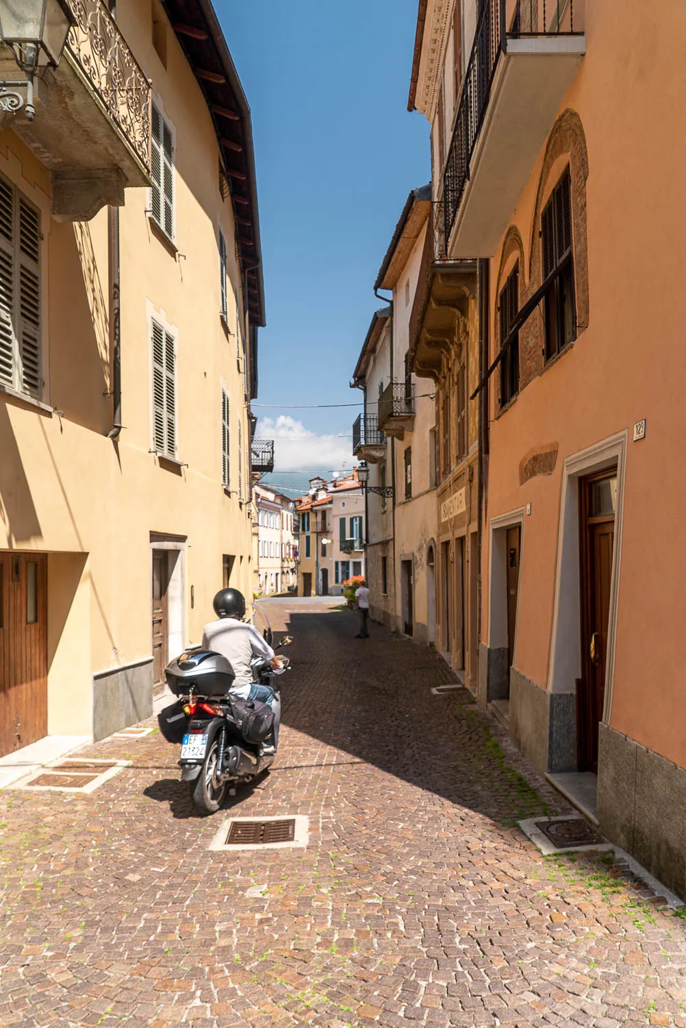 Motorradfahrer fährt durch engen Steinpflasterweg zwischen historischen Häusern.