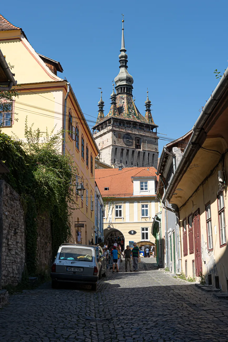 Giebelhäuser flankieren eine steinpflasterte Gasse mit Turm im Hintergrund.