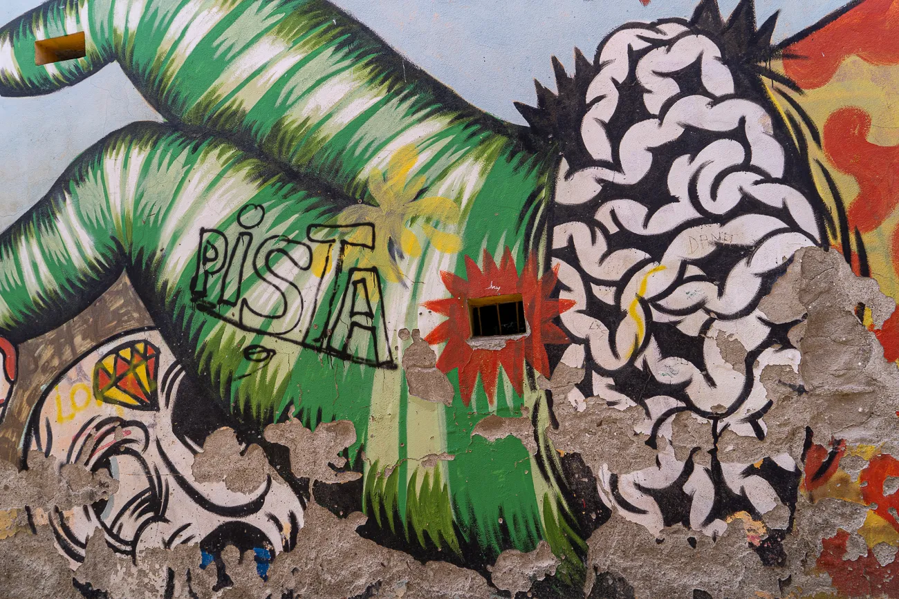 Farbenfrohes Graffiti an einer verwitterten Wand mit stilisierten Formen und dem Wort Pista.
