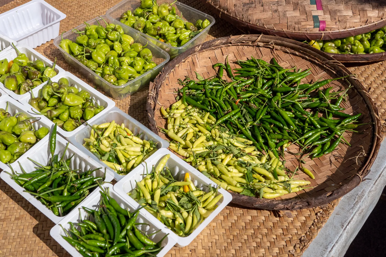 Grüne Chilis in Schalen und Körben auf einem Marktstand