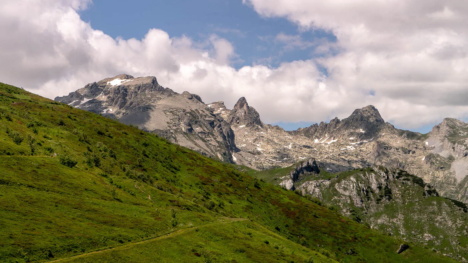Grüne Hügellandschaft mit steilen Bergen im Hintergrund unter bewölktem Himmel