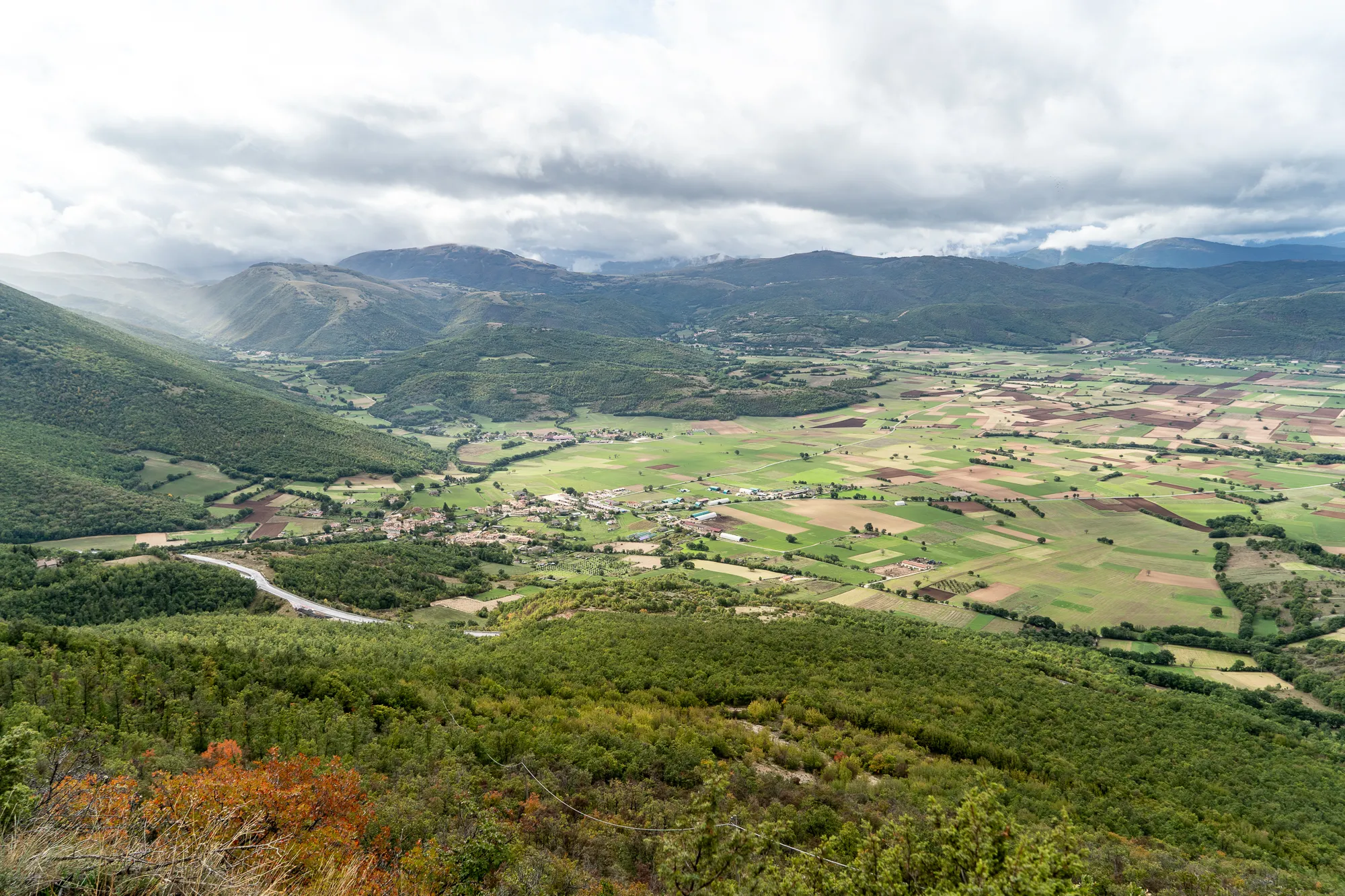 grün bewaldete hügel und tälern mit ackerflächen und dorf unter bewölktem himmel