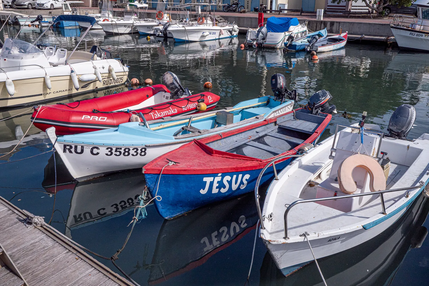 Boote liegen im Hafen, einige mit Namen wie Jesus und Takamaka.