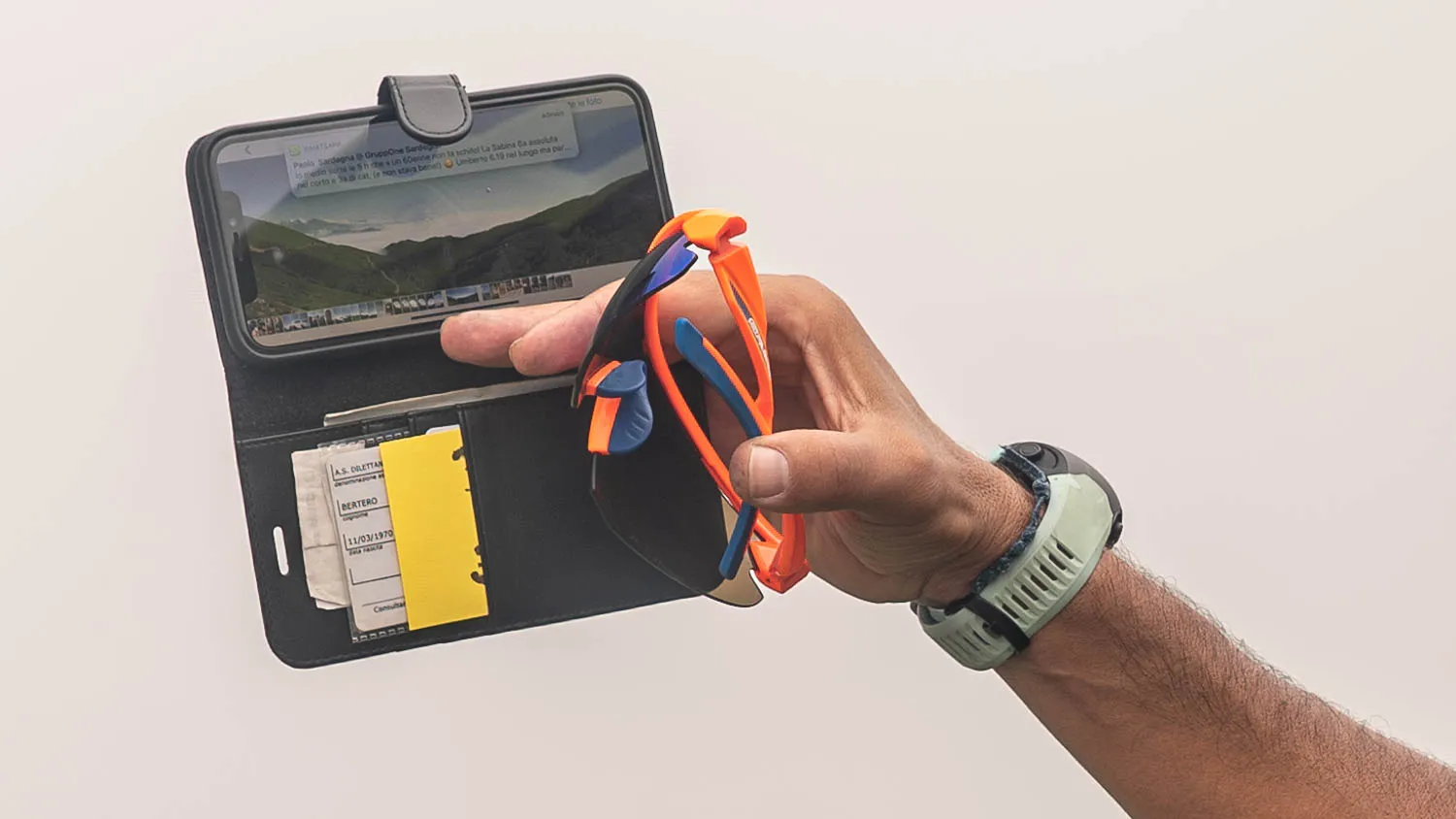 Hand hält Sonnenbrille und Handy mit Berglandschaft auf Display