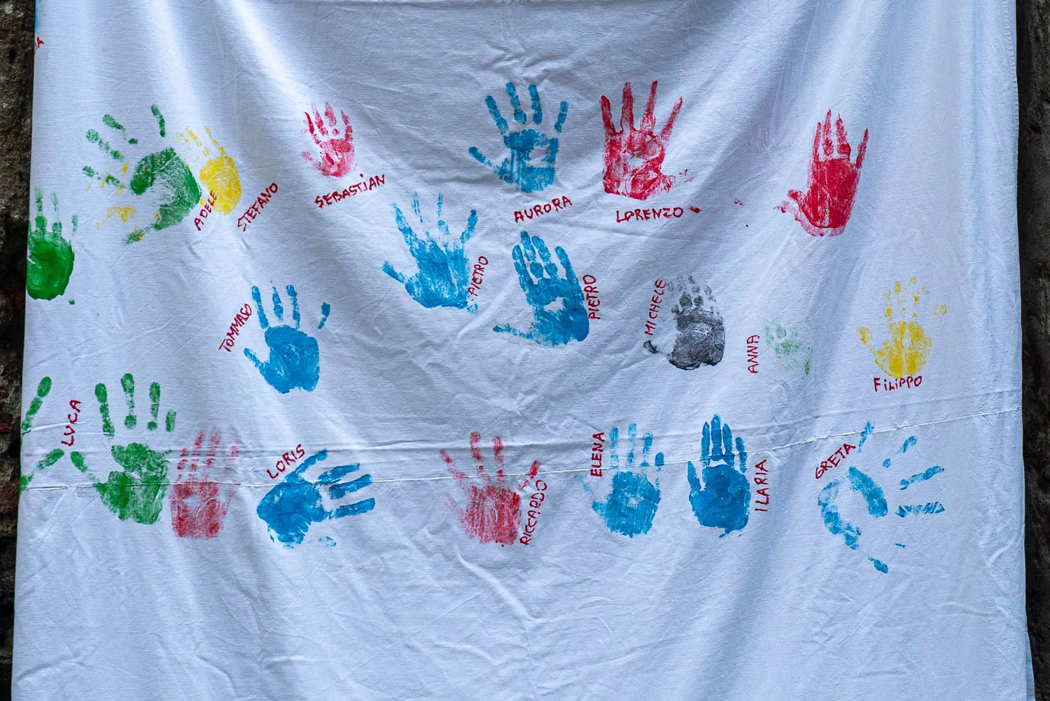Bunte Kinderhandabdruecke auf weißem Stoff mit Namen