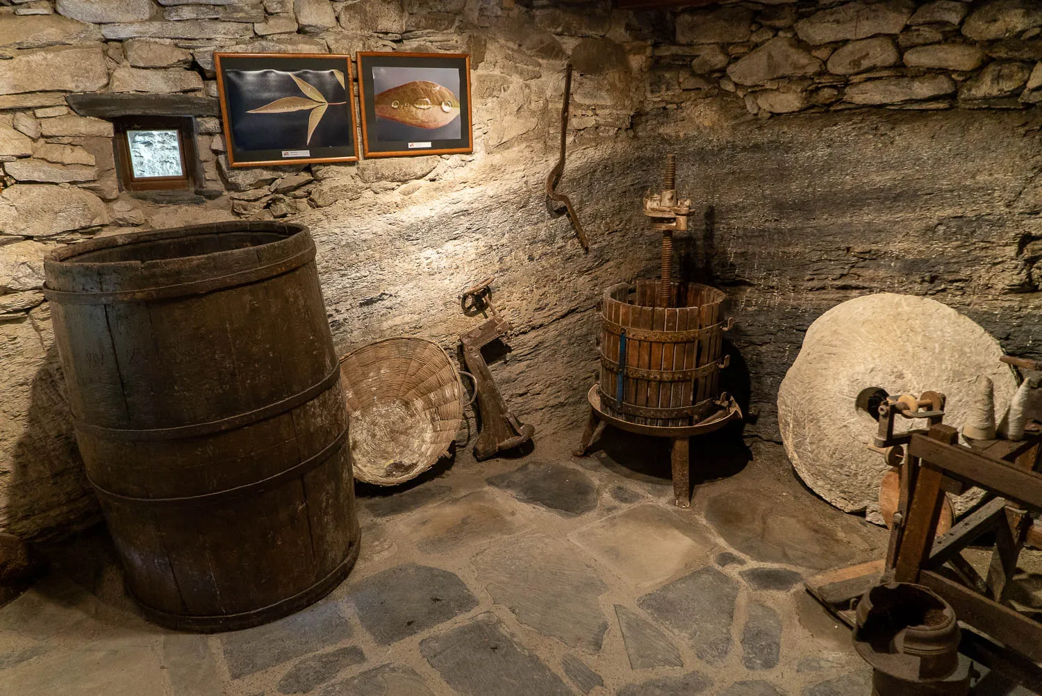 Holzfässer, Mühlenstein und traditionelle Geräte in Steinwandraum