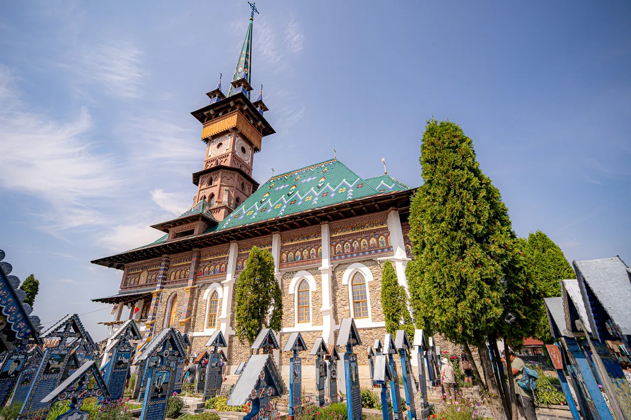 Holzkirche mit grünem Dach und blauen Grabsteinen im Vordergrund