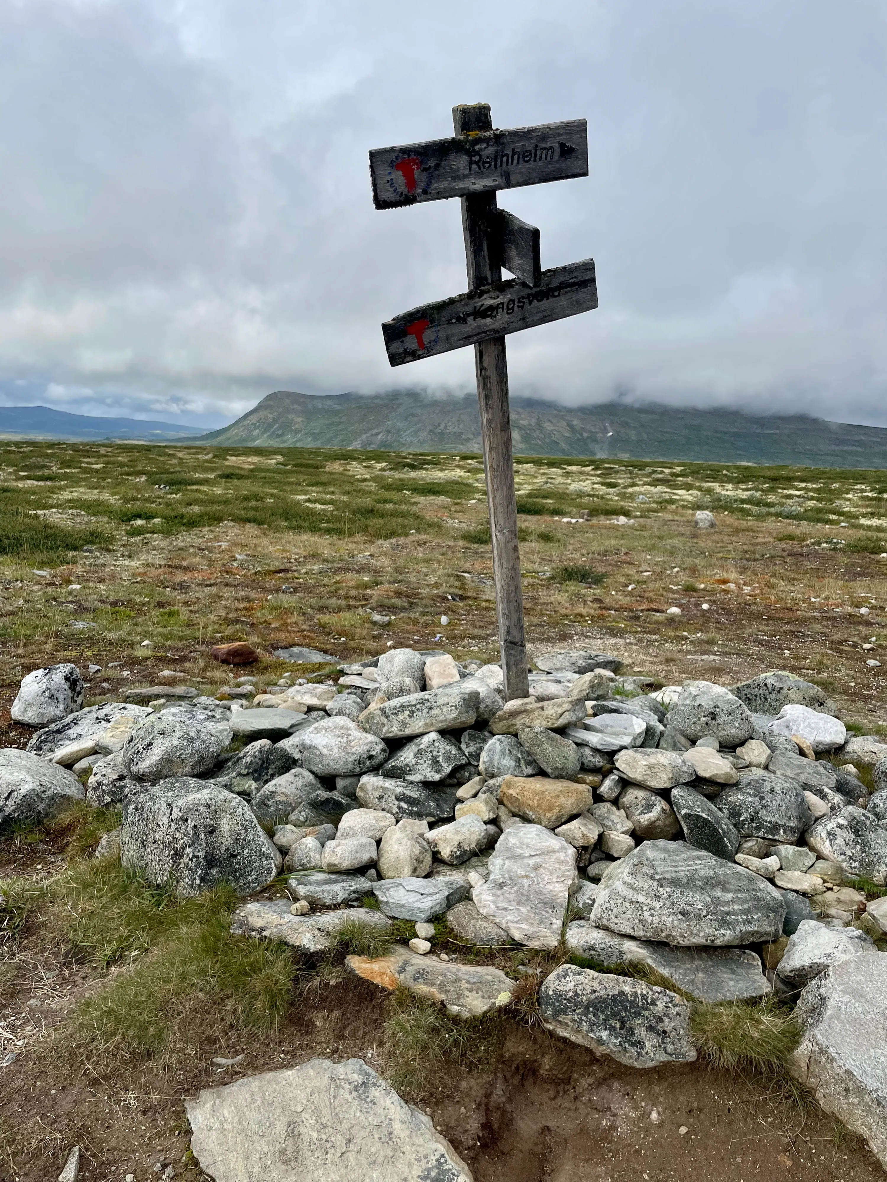 Holzschild mit Wanderwegweisern auf Steinhaufen in norwegischer Tundra