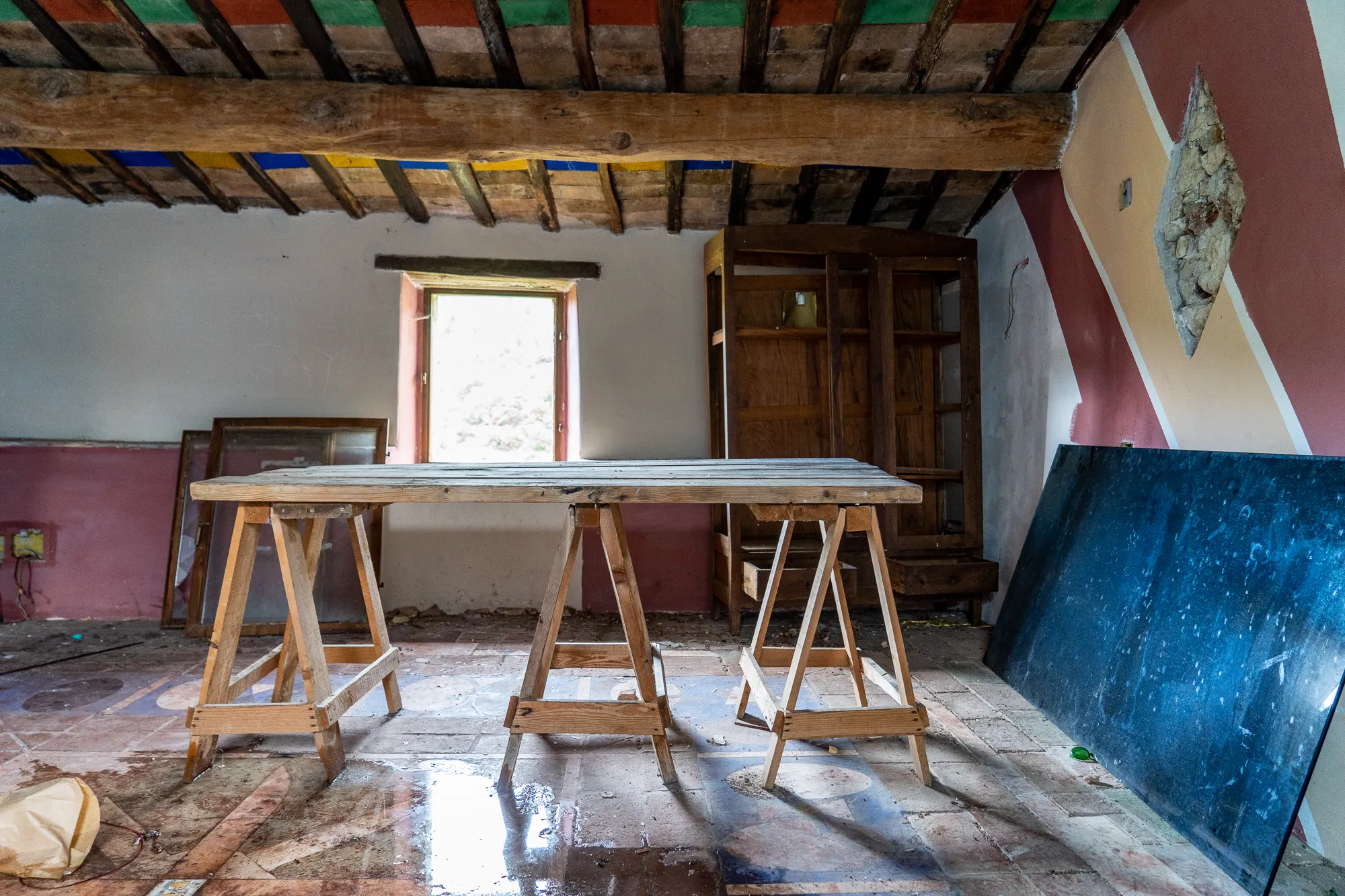 Holztisch auf Sägewerkschienen in einem verlassenen Raum mit farbigem Holzdeckenbalken.