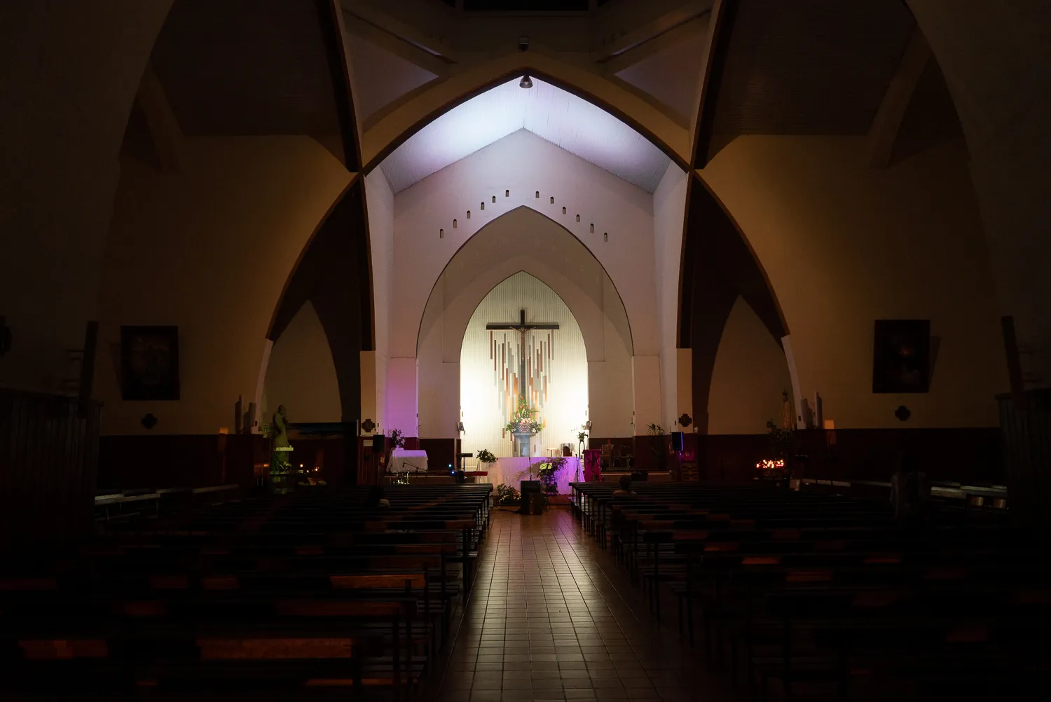Innenraum einer Kirche mit Bänken, Altar und beleuchtetem Kreuz