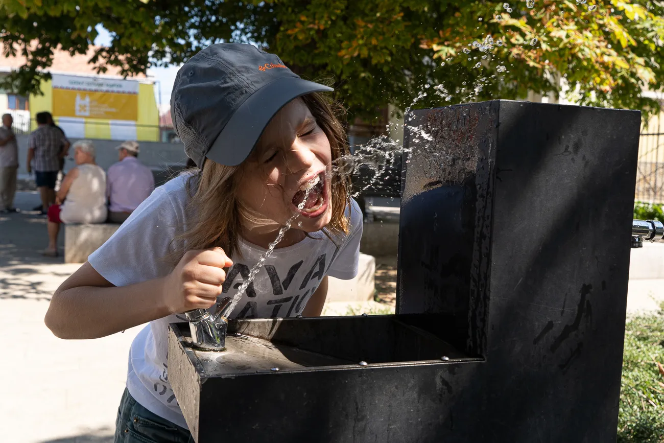 Kind trinkt aus einem Brunnen, Wasser spritzt aus dem Mund.