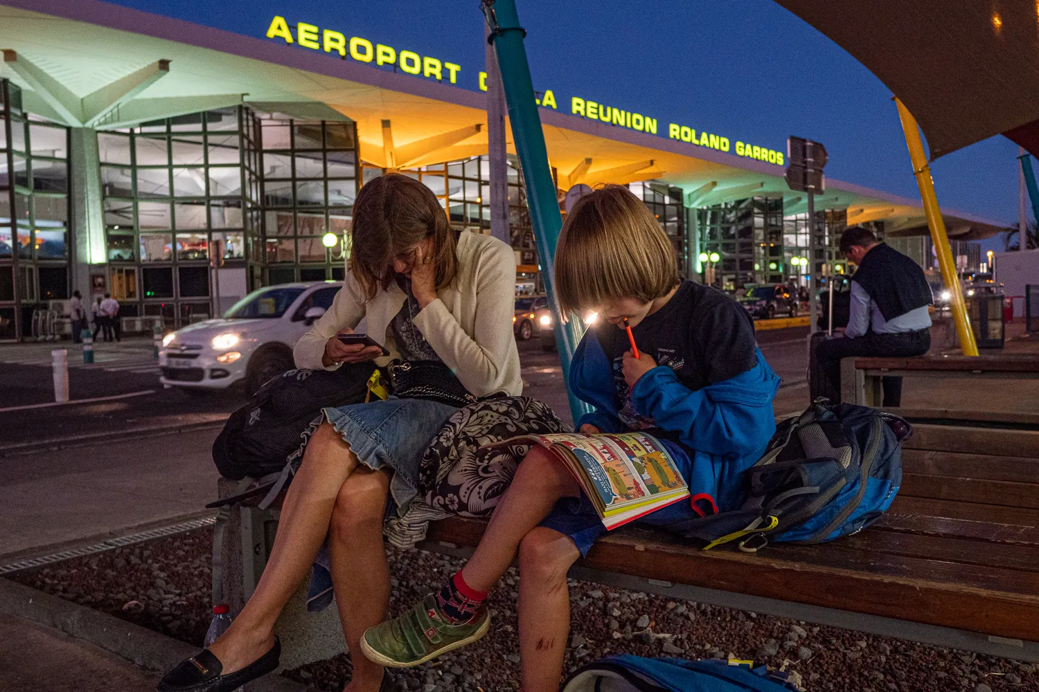 Zwei Kinder sitzen am Flughafen von La Réunion und schauen in ihre Bücher.