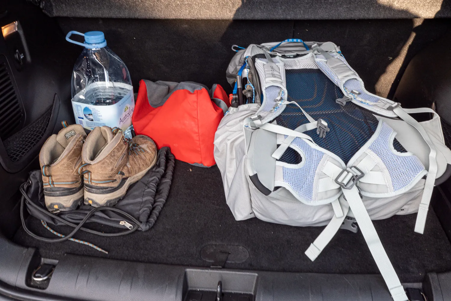 Rucksack, Wanderschuhe und Wasserflasche im Kofferraum eines Autos