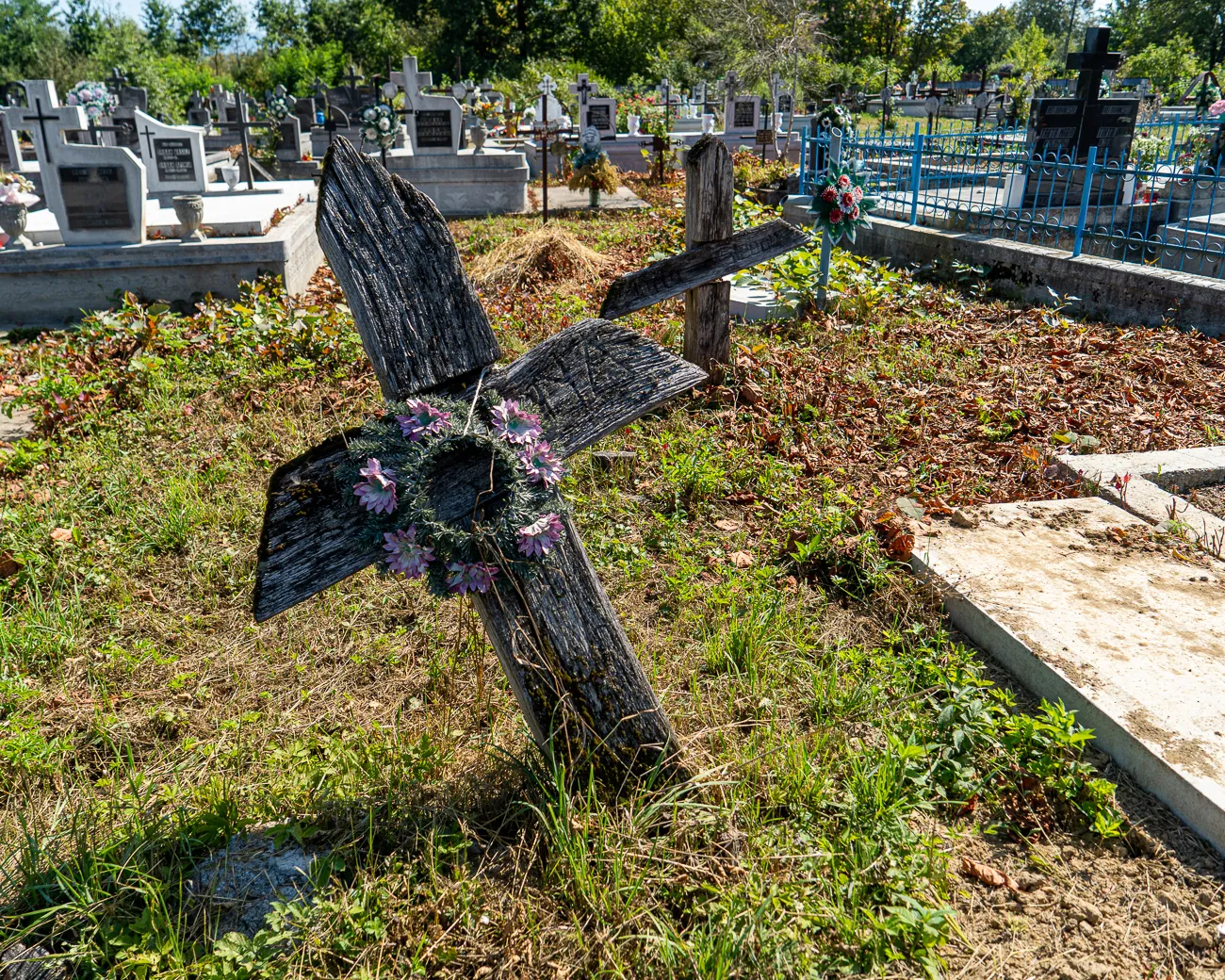 Holzkreuz mit Blumen auf einem Friedhof unter Bäumen