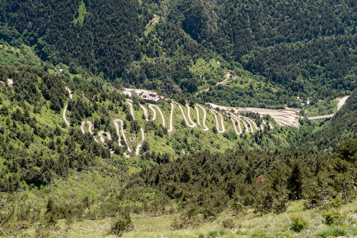 Winding road through green mountains with buildings at the bend