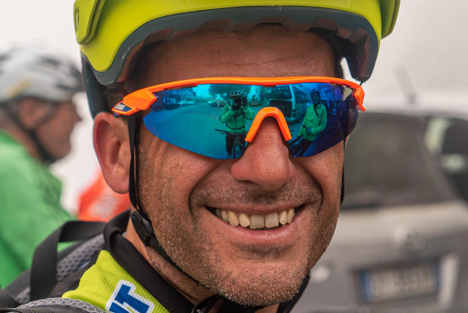 Radfahrer mit gelbem Helm und orangefarbenen Sonnenbrille lächelt in die Kamera.