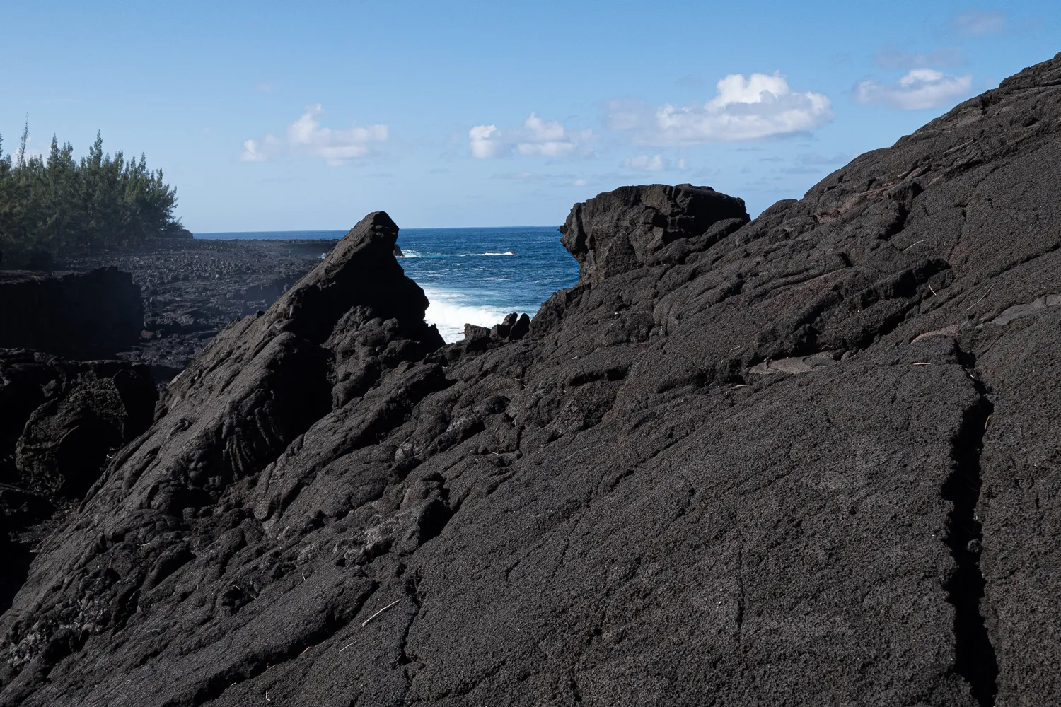 Schwarze Lavasteine am Strand mit blauem Meer und bewölktem Himmel