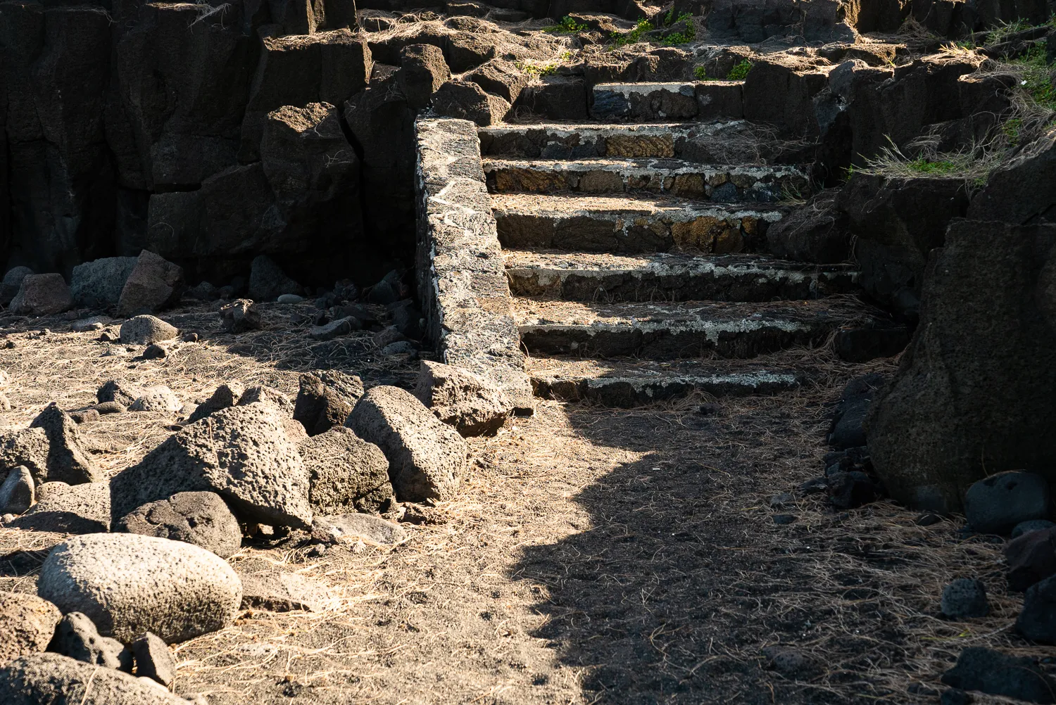 Steinige Treppe durch Lavastromlandschaft mit Felsblöcken und trockener Vegetation