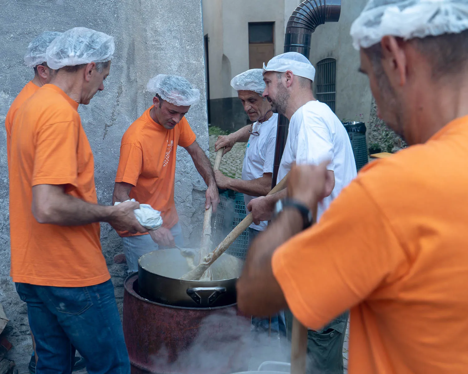 Männer in orangefarbenen T-Shirts kochen in einer großen Pfanne auf der Straße.