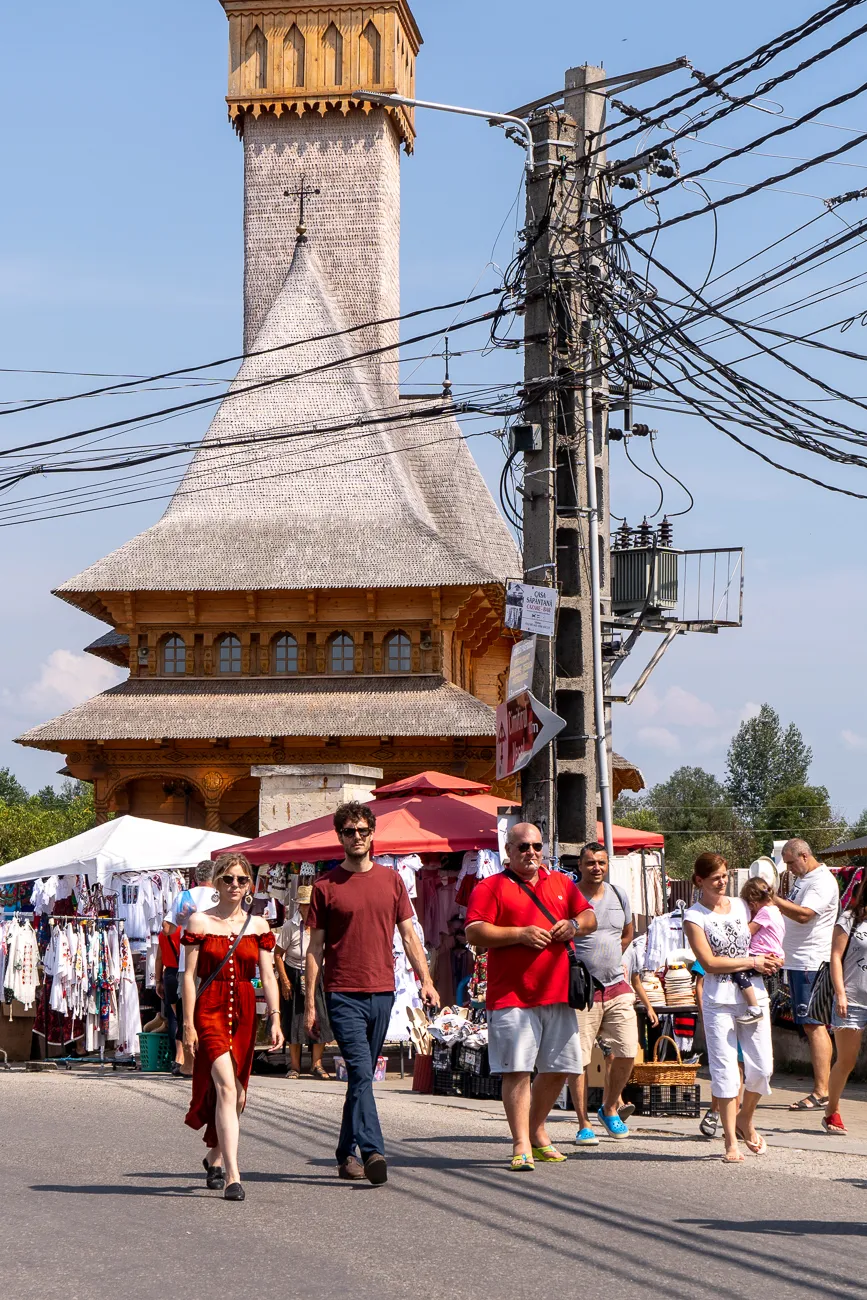 Markt vor Holzkirche mit Besuchern und Strommasten