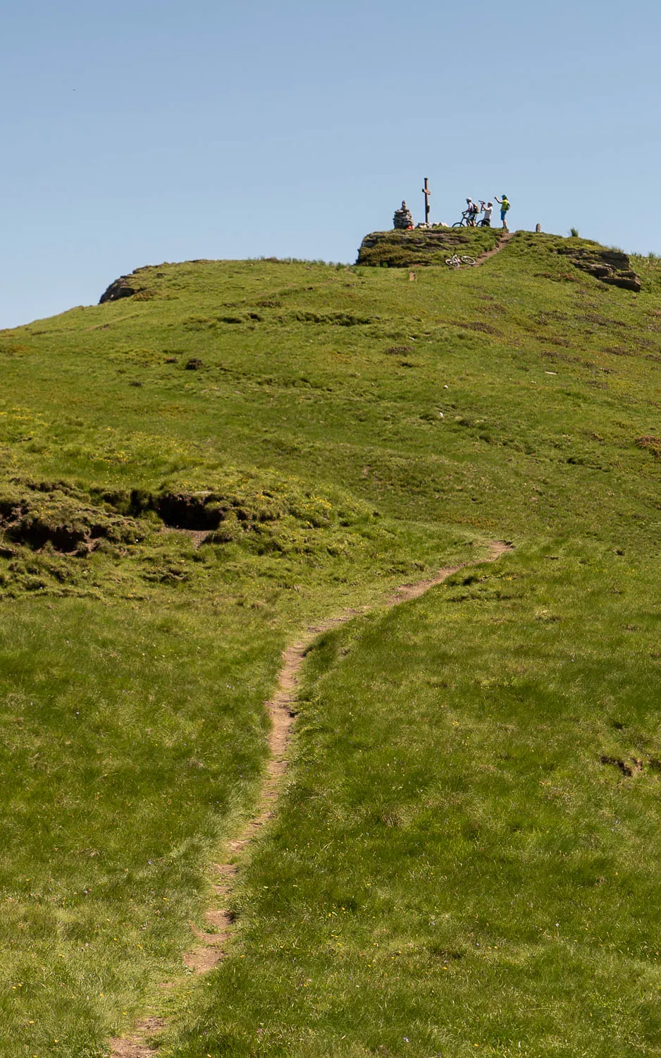 Menschen stehen auf grüner Bergkuppe unter blauem Himmel