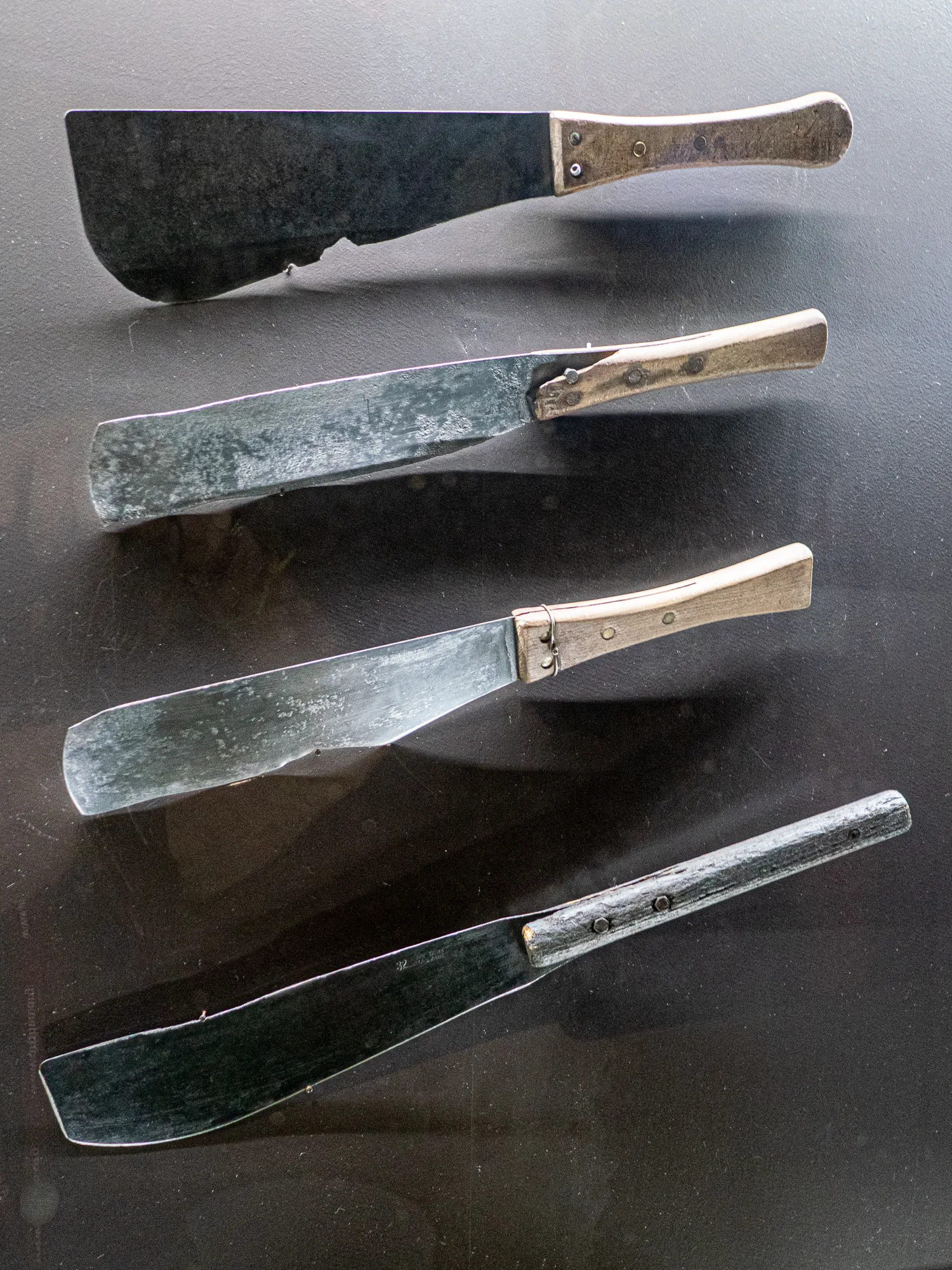 Vier alte Messer mit Holzgriffen liegen auf dunkler Oberfläche.
