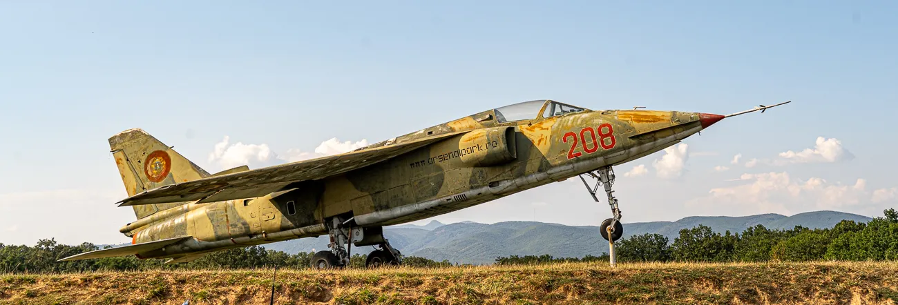 verlassenes militärisches Flugzeug auf Feld mit Bergen im Hintergrund