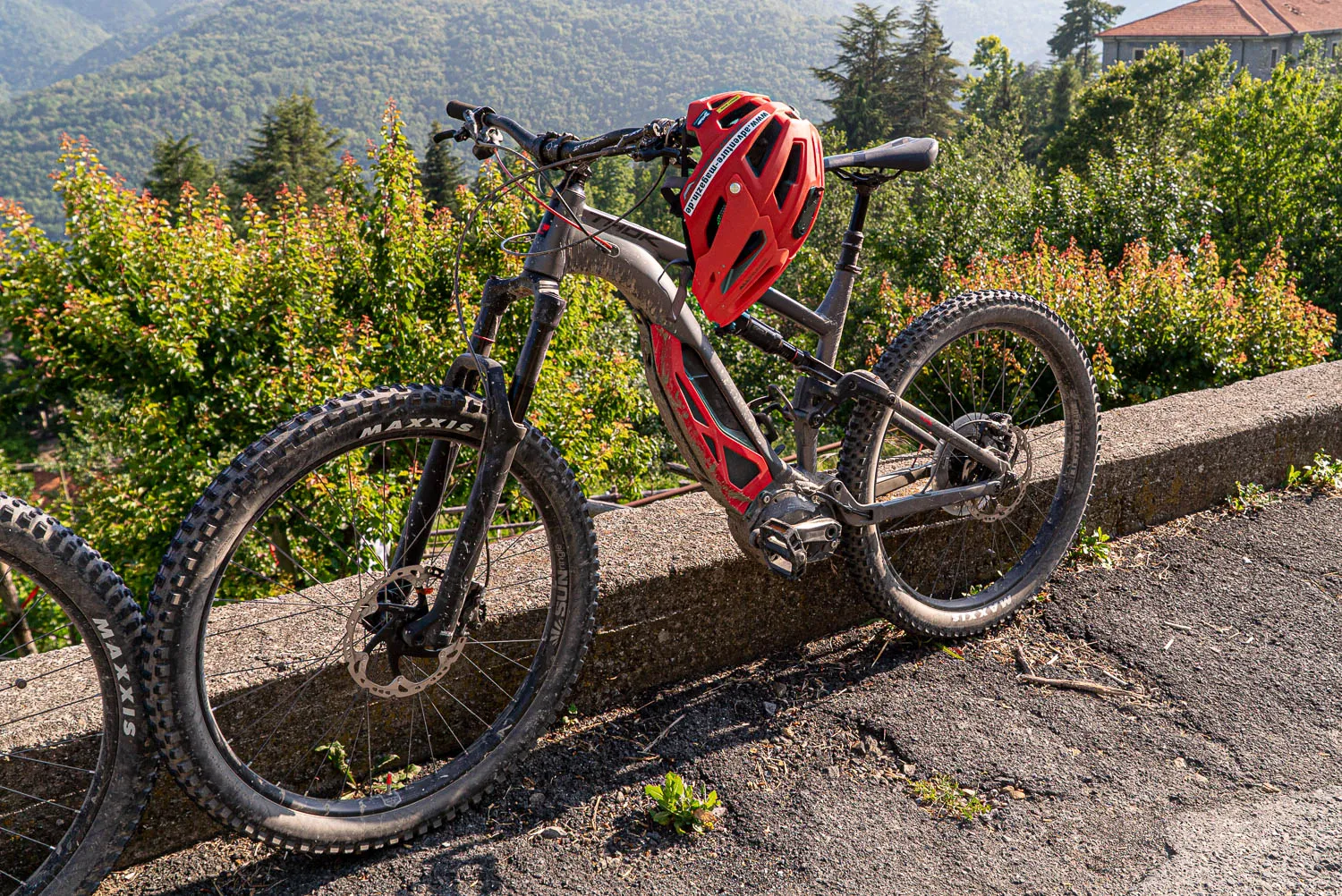 Rote Mountainbike mit Helm lehnt an Steinmauer vor grüner Landschaft