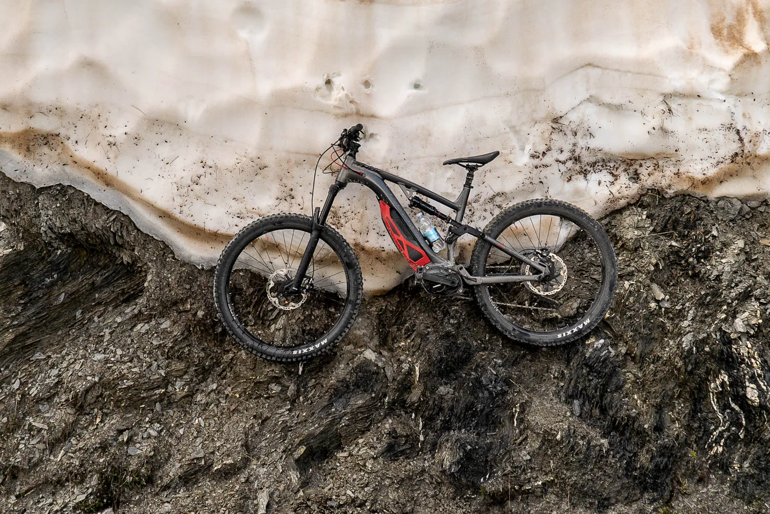 Mountainbike lehnt an Schneewand auf felsigem Untergrund