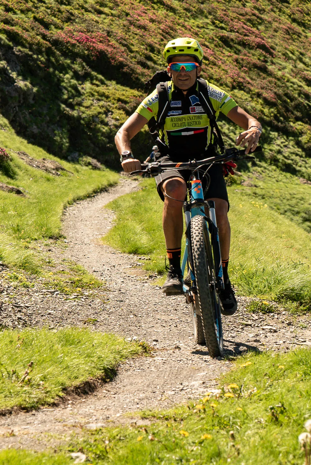 Mann fährt Mountainbike auf steinigem Pfad durch grüne Hügellandschaft