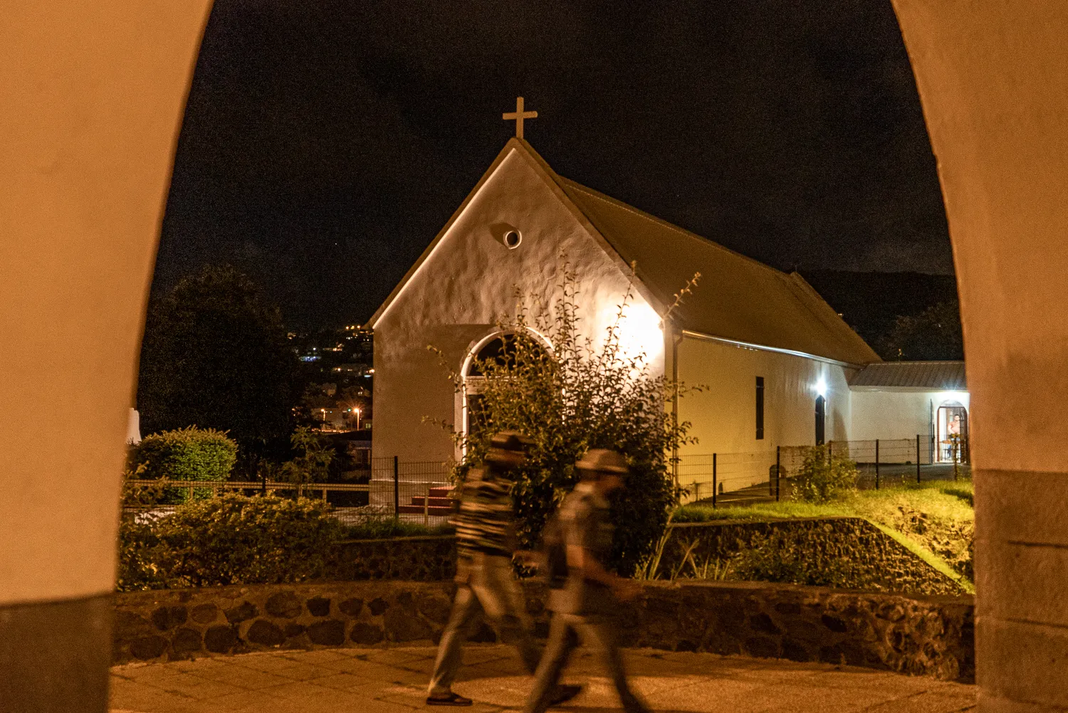 Beleuchtete Kirche bei Nacht mit zwei vorbeigehenden Personen