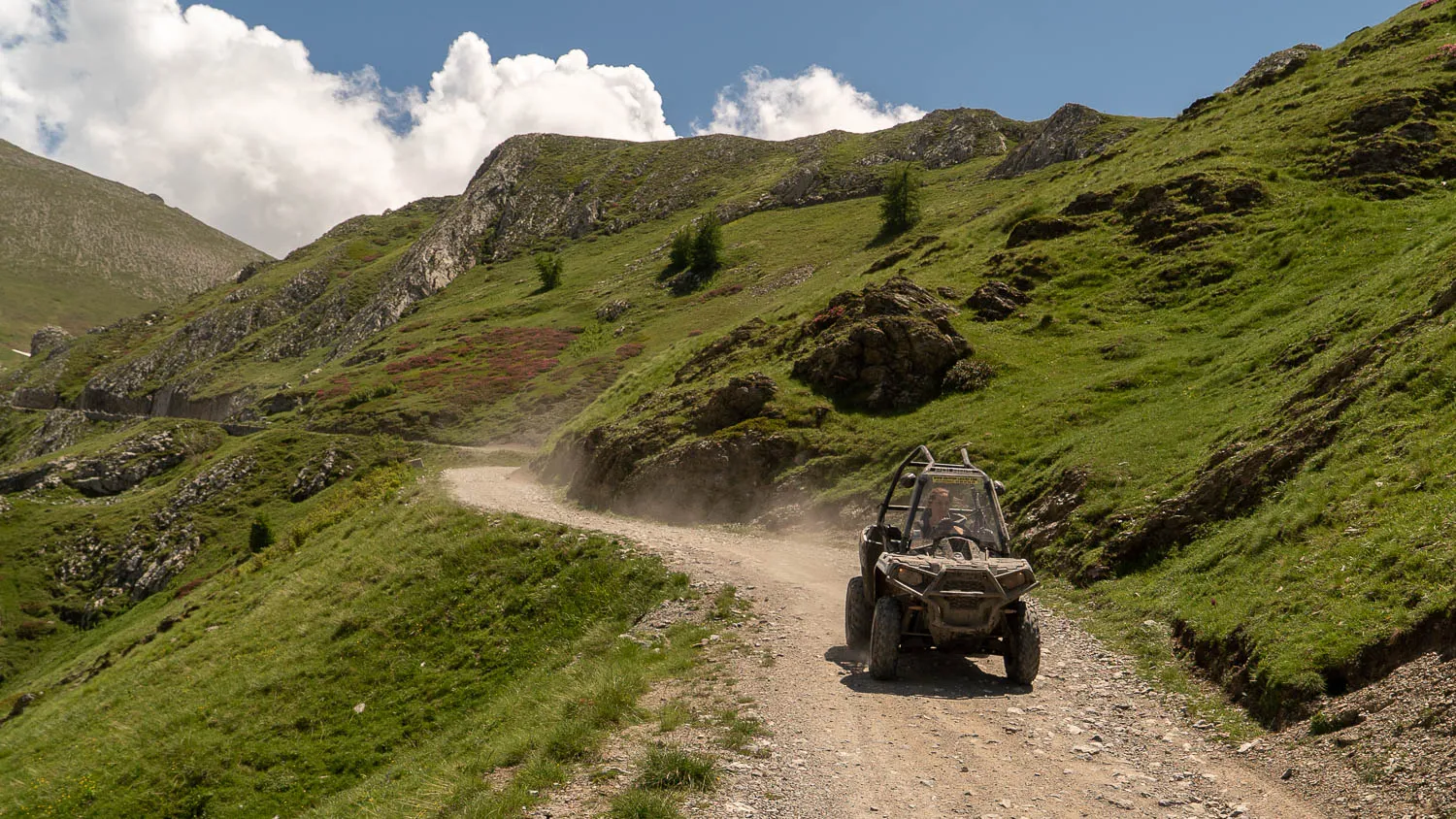 Offroad-Fahrzeug auf steinigem Pfad in grüner Berglandschaft