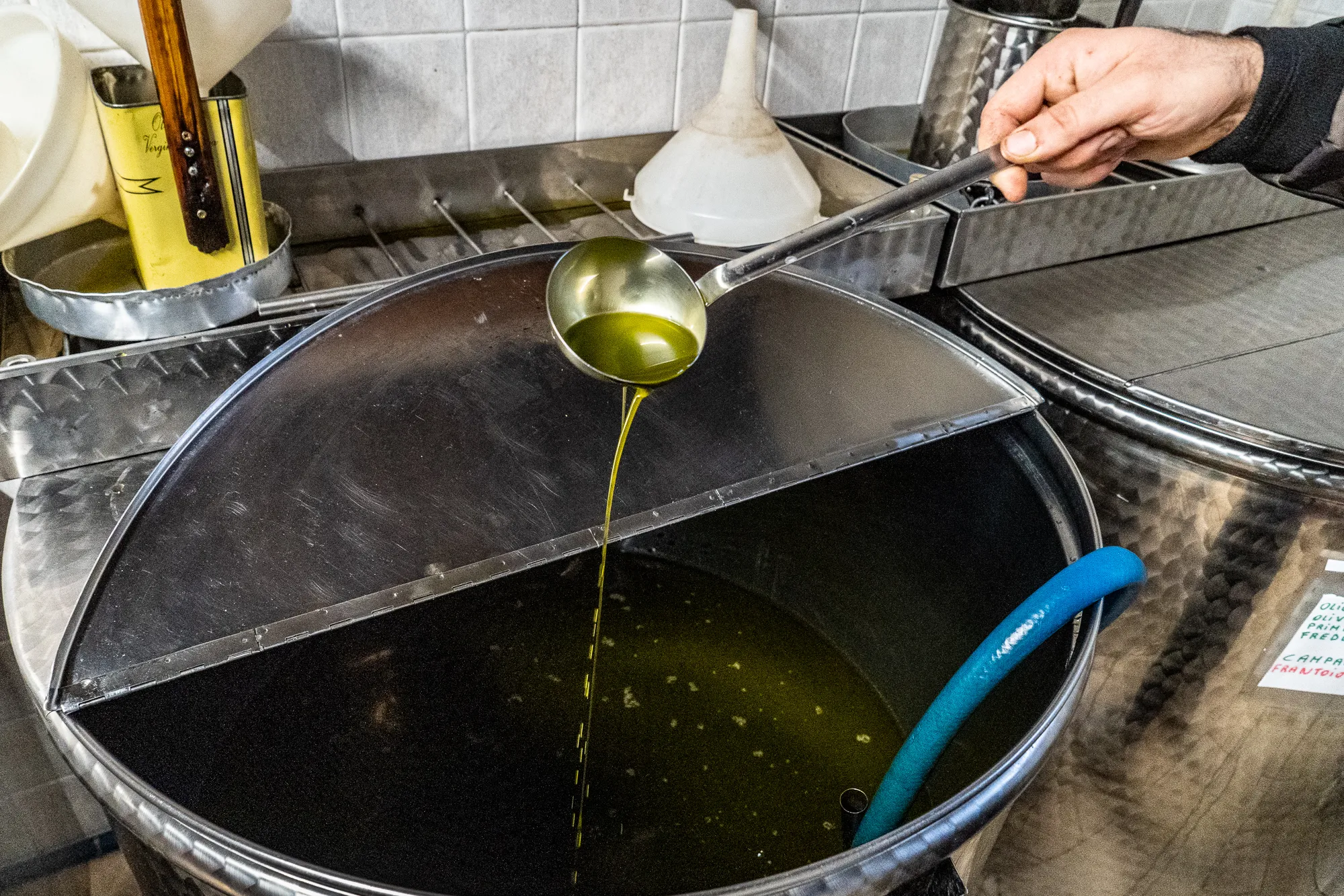 Hand gießt Olivenöl aus Löffel in große Metalltonne