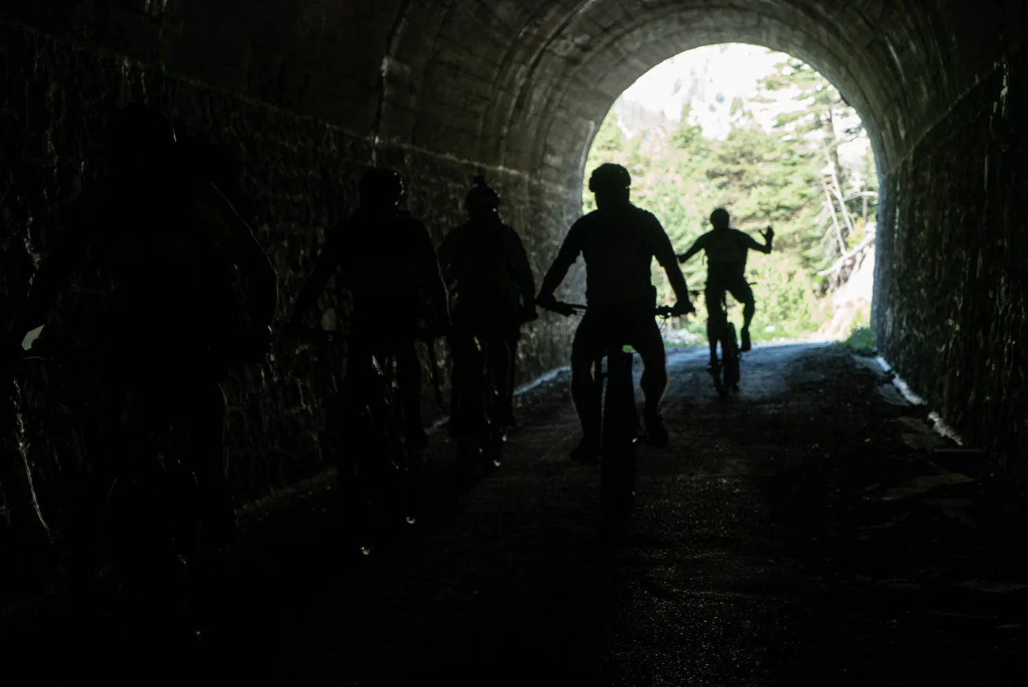 Fahrradfahrer fahren durch einen dunklen Stein tunnel mit grünem Wald am Ende.