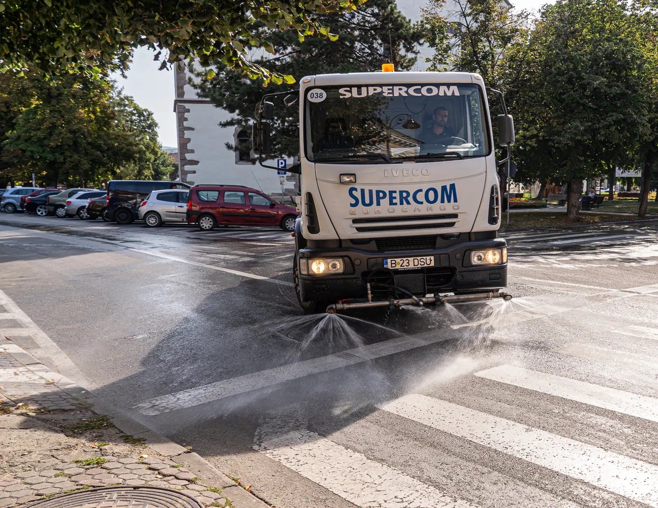 Straßenreinigungswagen spült Zebrastreifen mit Wasser.