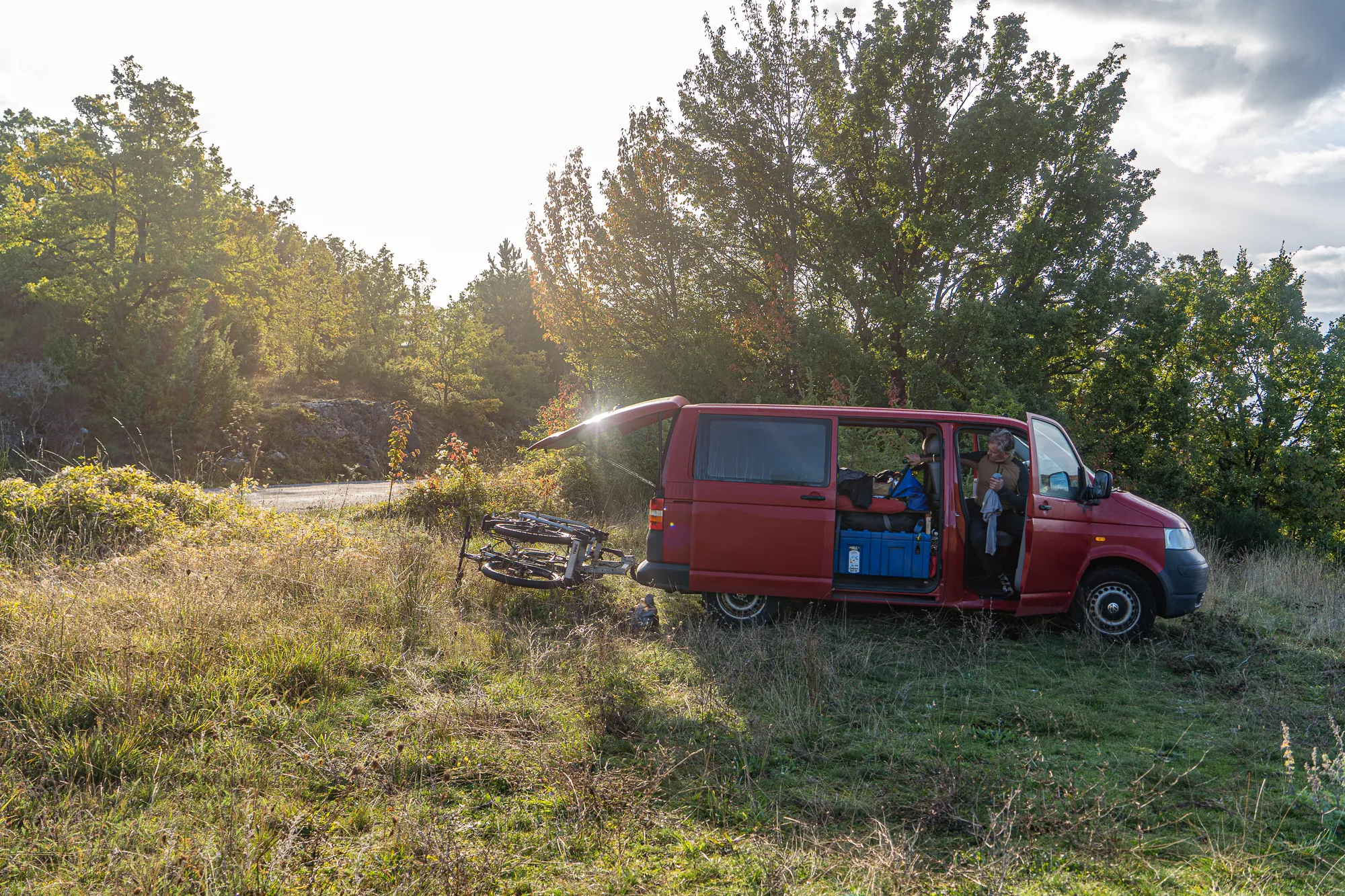 Roter Van mit geöffneten Türen auf grünem Hügel mit Bäumen im Hintergrund.