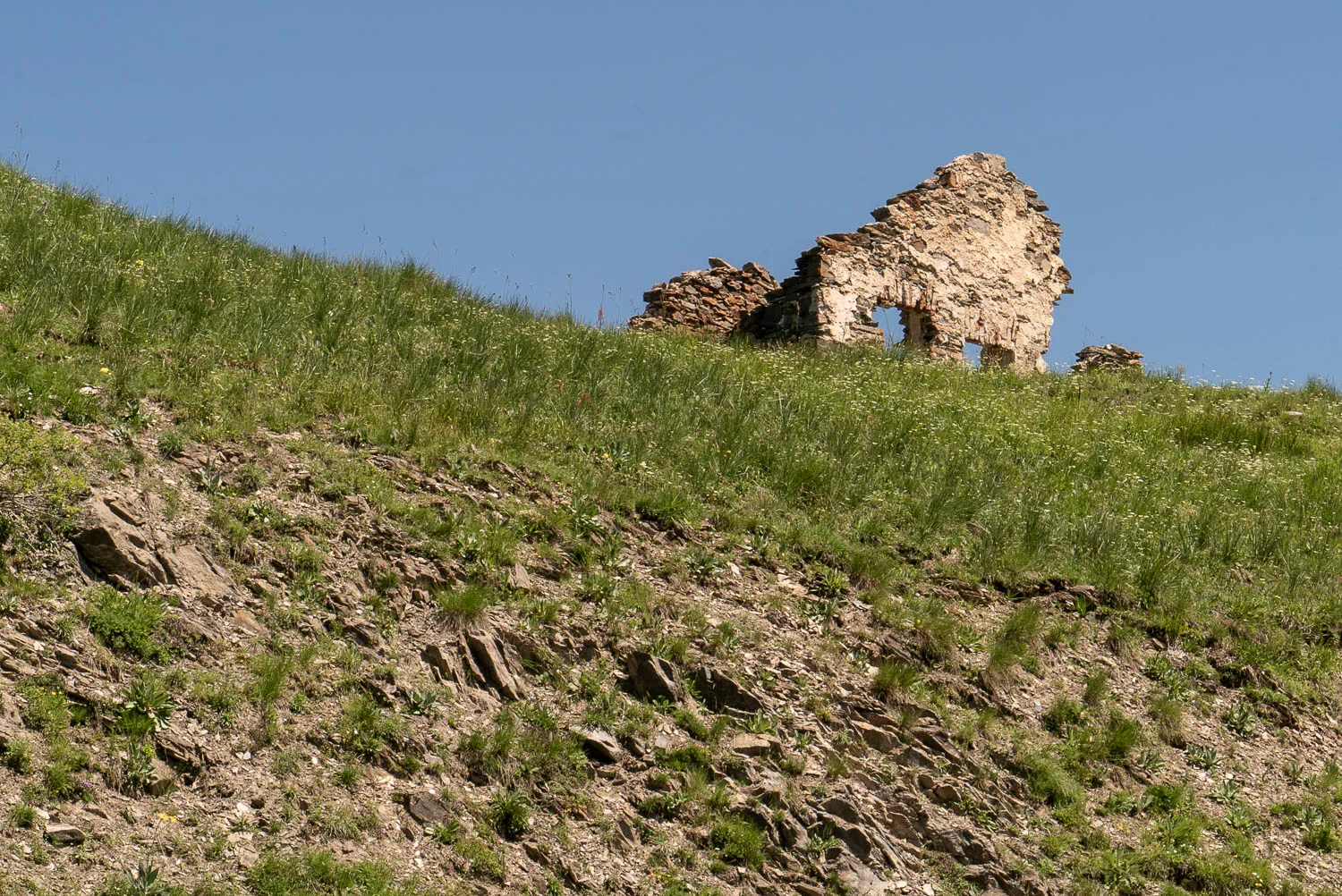 Ruinen auf grüner Hanglage unter blauem Himmel
