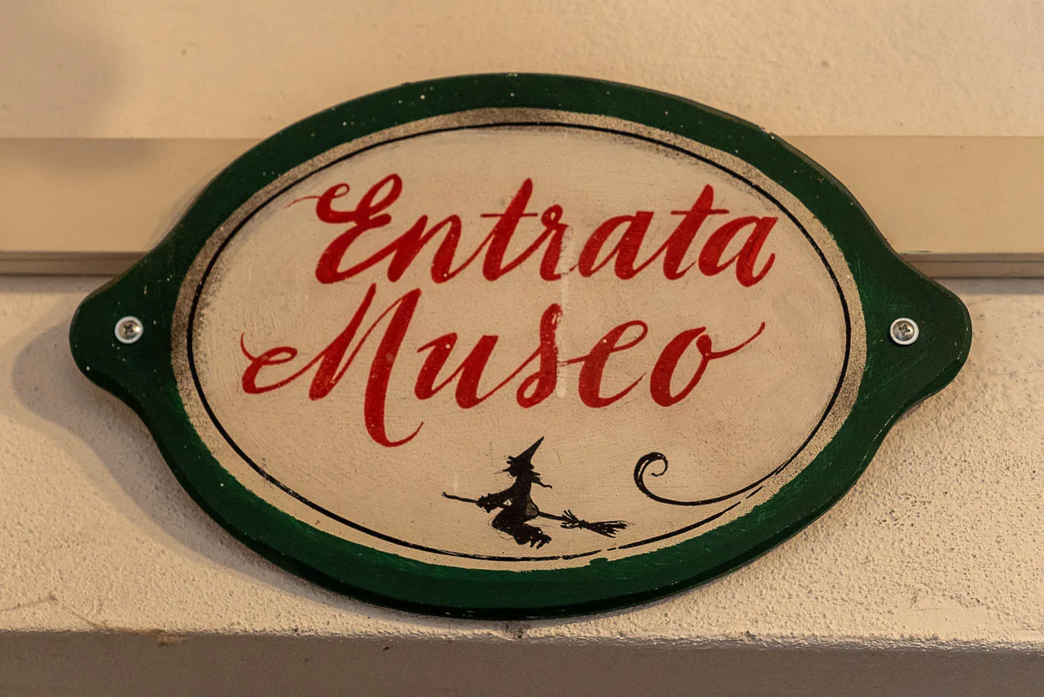 Schild mit roter Schrift und Hexe auf Besen